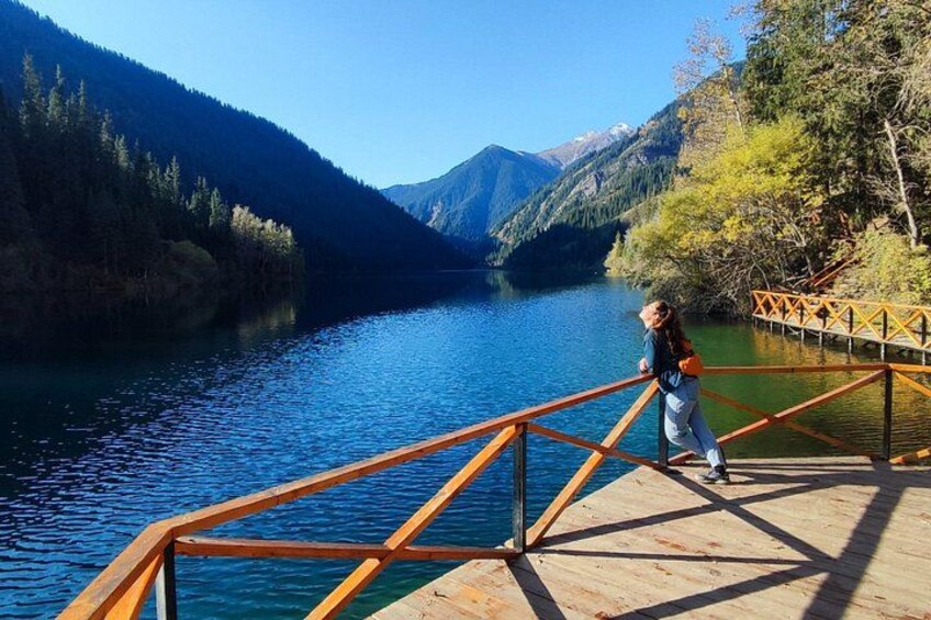 A wooden dock extending over a calm lake surrounded by forested mountains. 1