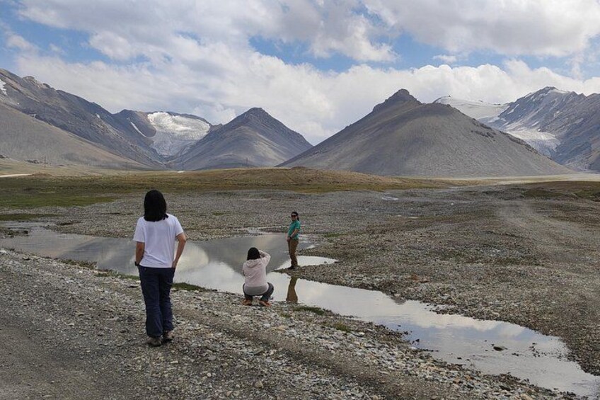 A group of people standing and sitting on a rocky terrain with mountains in the background. 3