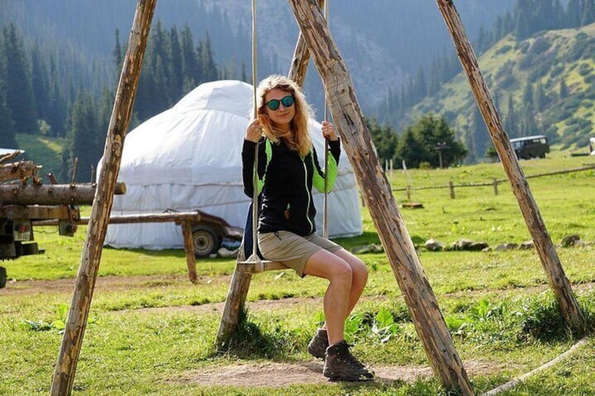 A person sitting on a swing in a grassy field with mountains in the background. 1