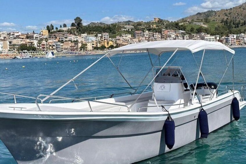 A white motorboat with a canopy, anchored near a coastal town with buildings and hills in the background. 3