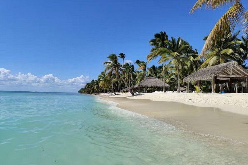 A beach with clear turquoise water, white sand, palm trees, and thatched-roof huts. 2