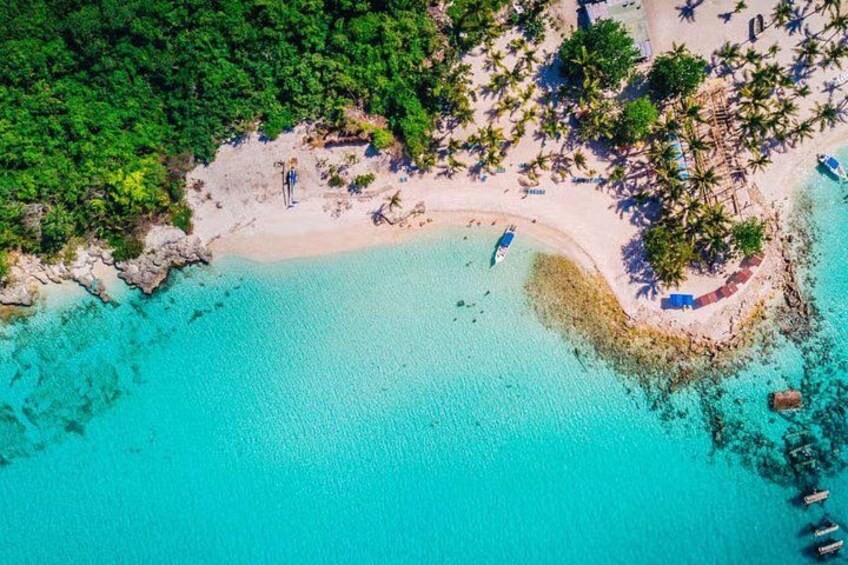 An aerial view of a turquoise beach with clear waters, palm trees, and a few boats. 3