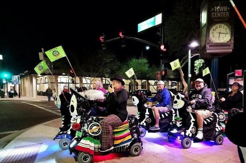 People riding decorated scooters on a sidewalk at night. 3