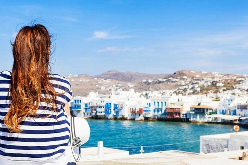 A person with long hair sitting by a waterfront with colorful buildings in the background. 2
