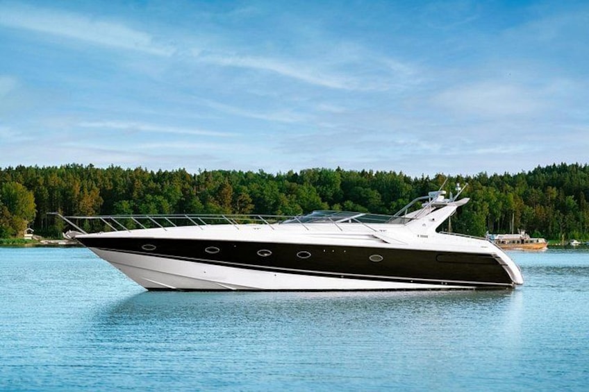 A white and black motor yacht on calm water with a forested shoreline in the background. 1