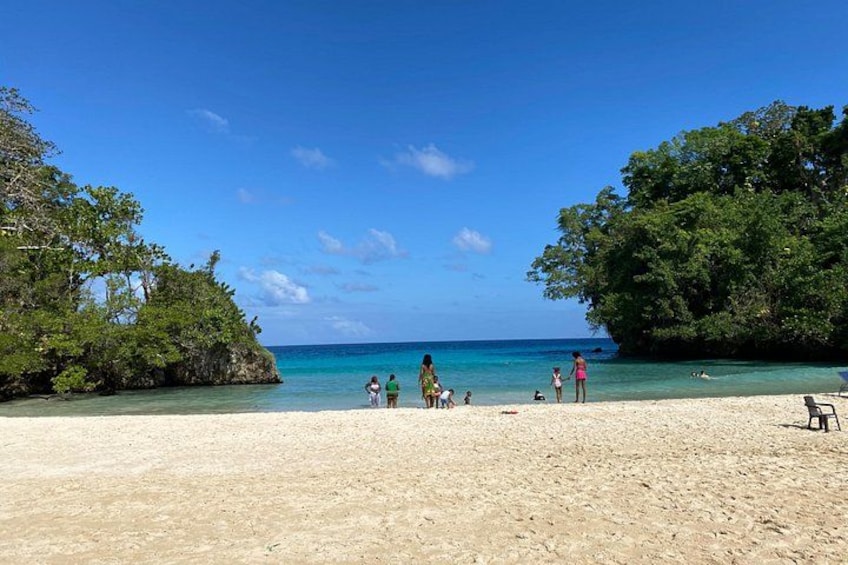 A beach with clear turquoise water, people walking, and lush green trees. 2