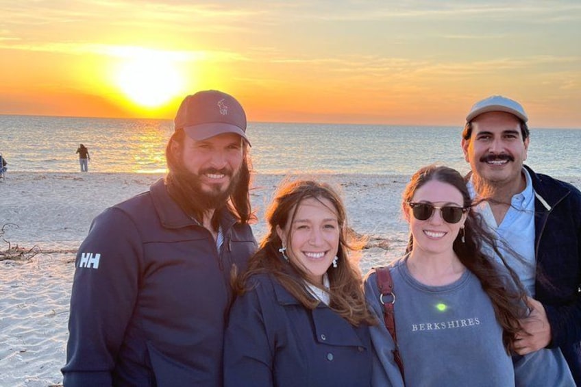 A sunset over a beach with people standing on the sand. 1