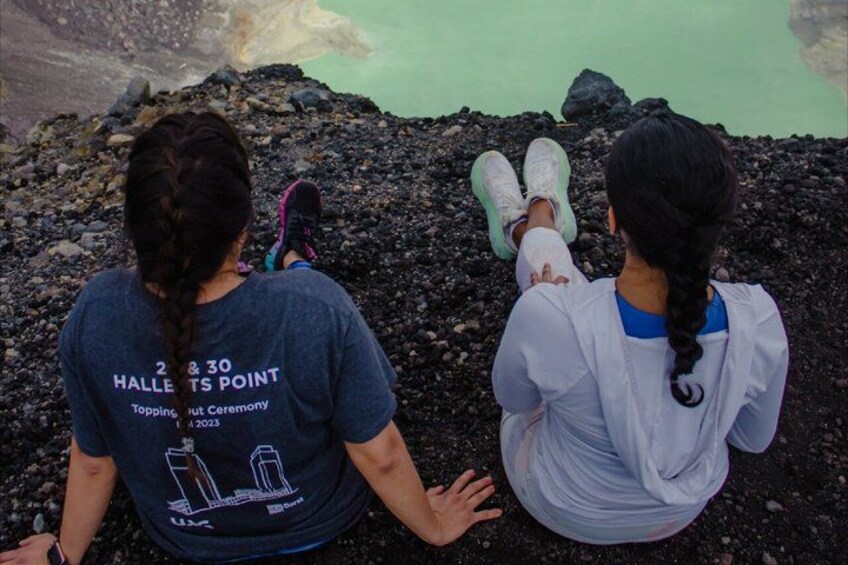 Two people sitting on a rocky shore with a body of water in the background. 2