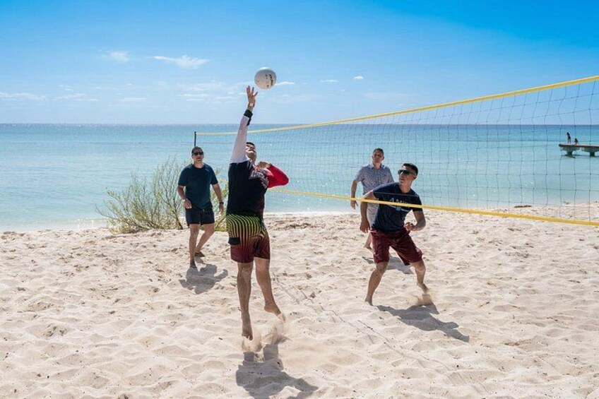 En strandvolleybollmatch med spelare i full fart, ett volleybollnät och en klar himmel. 3