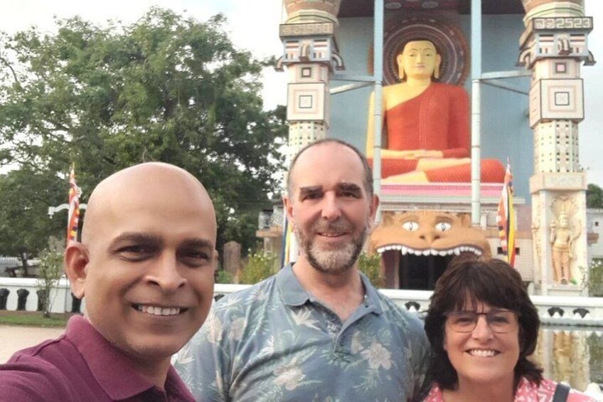 Three people in front of a large Buddha statue with a temple structure behind them. 3