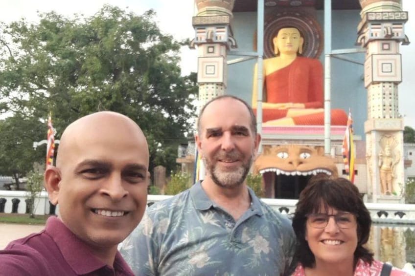 Three people in front of a large Buddha statue with intricate architecture. 2