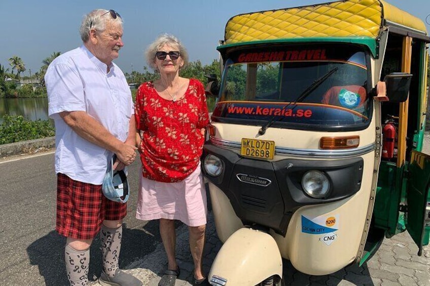 Two people standing next to a yellow and beige auto-rickshaw with a website address on the windshield. 1