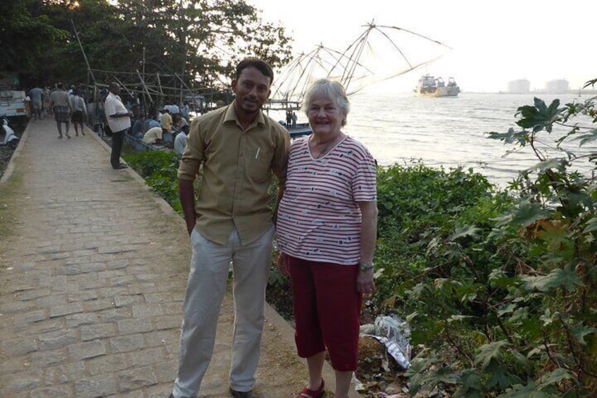 Two people standing on a stone pathway by a river with fishing nets in the background. 4