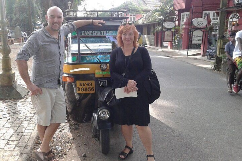 A man and a woman standing next to a Ganesha Travel auto-rickshaw on a street. 3
