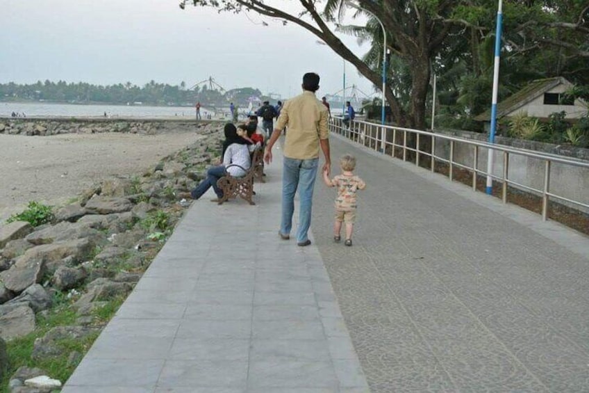 A man walking with a child on a paved walkway beside a beach. 2