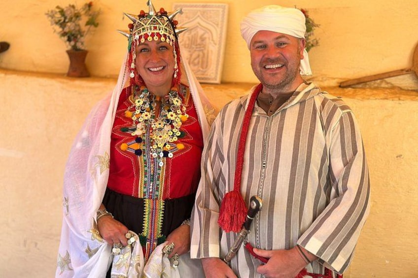 Une personne vêtue d’un costume traditionnel, portant une couronne et des bijoux, se tient à côté d’une autre personne qui porte un t-shirt à rayures. 5