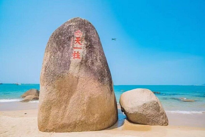 A large rock with Chinese characters, a smaller rock, and a clear blue sky with a plane in the distance. 5