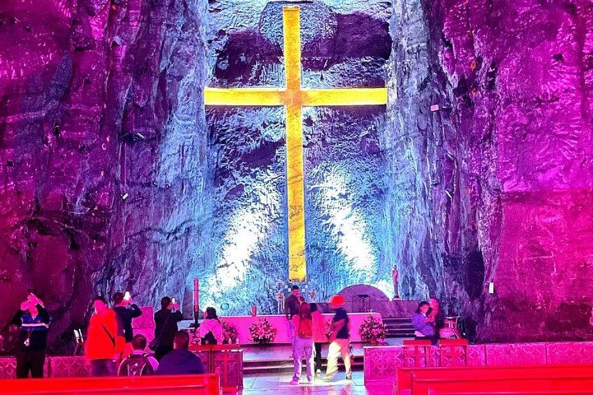 A large cross in a cave with people gathered around. 1