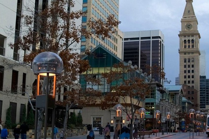 Una calle urbana con edificios modernos, una torre del reloj y árboles otoñales. 5