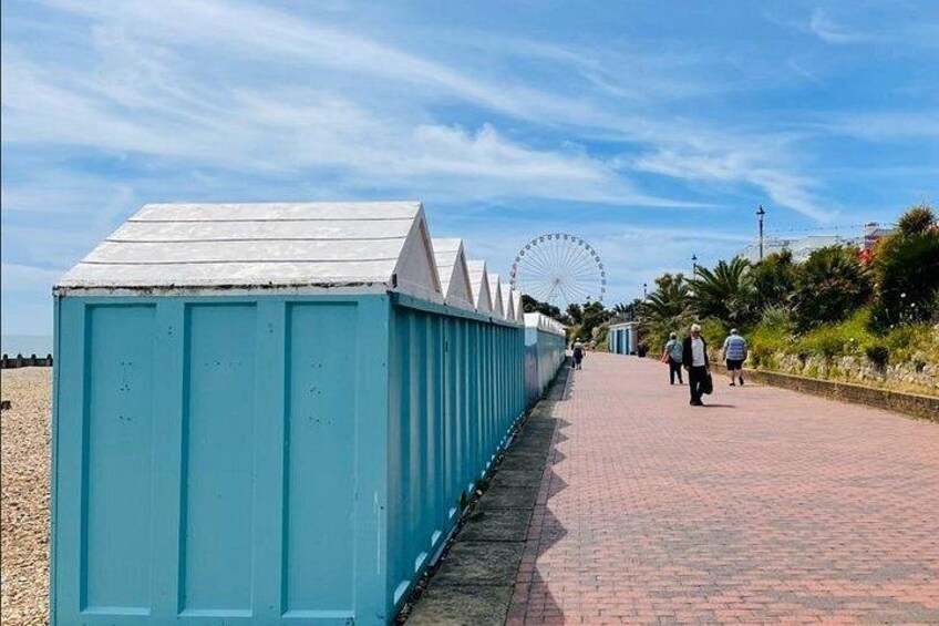 A seaside promenade with a row of blue structures, a Ferris wheel, and people walking. 4