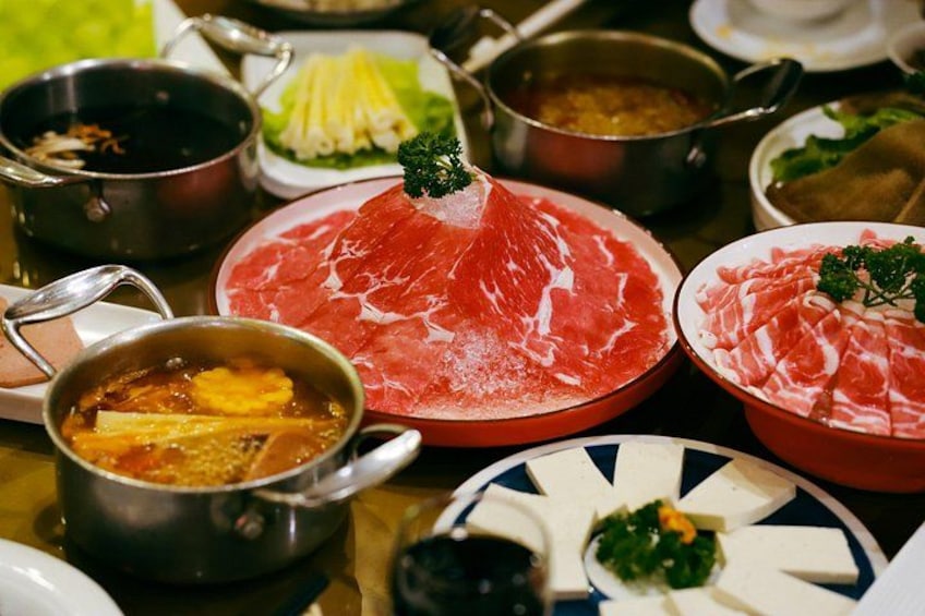 A table with various dishes including a large piece of raw meat, bowls of soup, and plates of food. 1