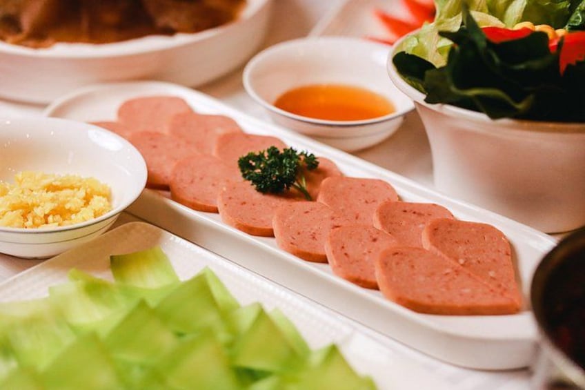 Sliced sausage, a bowl of mustard, and a salad on a table. 4
