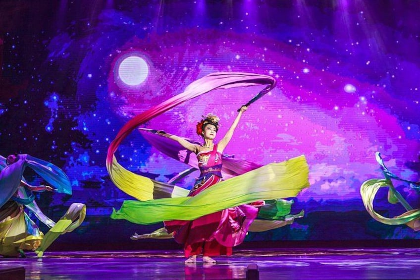 A performer in a colorful costume with flowing fabric, performing on a stage with a cosmic-themed backdrop. 5
