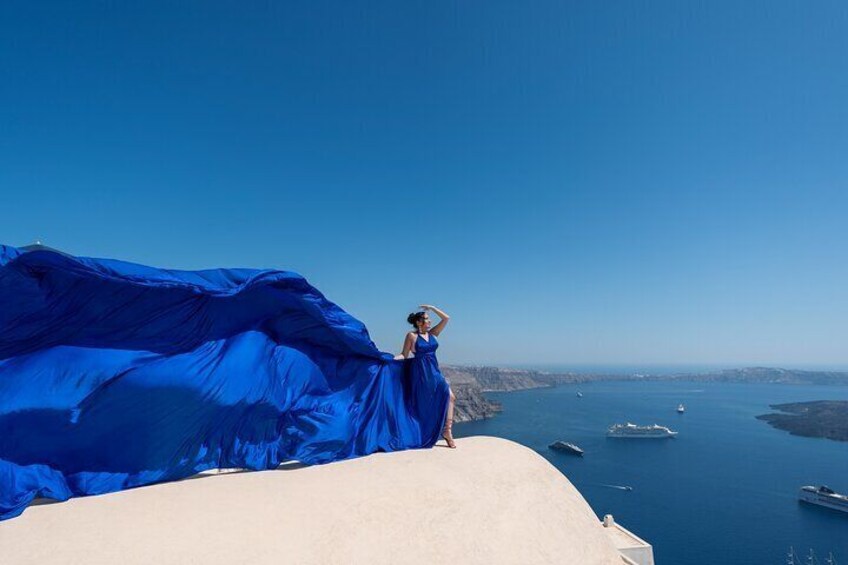 A person in a blue dress standing on a cliff overlooking a body of water with boats. 3