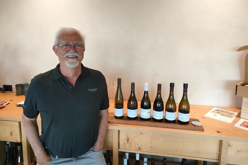 A man standing in front of a wooden table with several wine bottles. 4