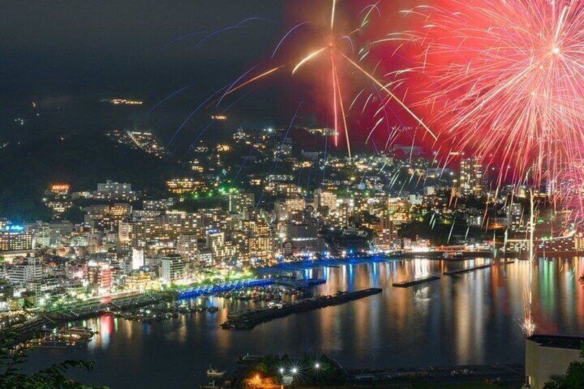 A cityscape at night with fireworks over a river and a bridge. 5