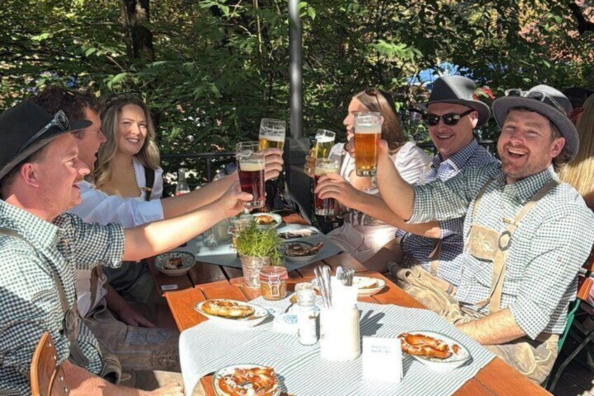 Un groupe de personnes trinquant avec des verres de bière autour d’une table en plein air, où se trouvent également des plats. 2