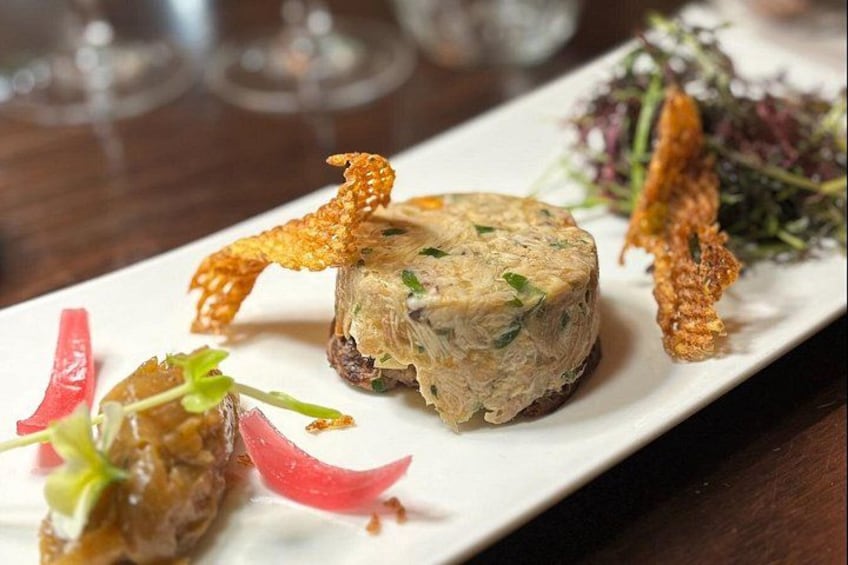 Un plat composé d’une terrine de viande ronde, décorée d’herbes fraîches et d’éléments croustillants, accompagnée d’une salade de jeunes pousses et de légumes marinés. 4