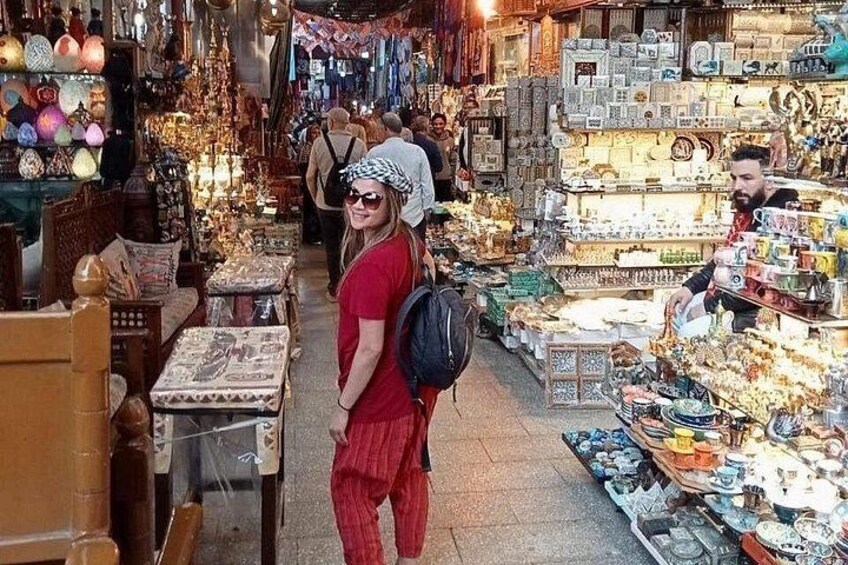 A crowded market with various stalls selling ceramics and textiles. 1