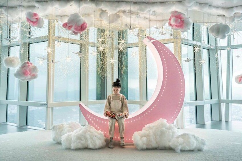 Una persona sentada sobre una decoración en forma de luna creciente en una habitación con ventanas amplias y esponjosas nubes blancas. 4