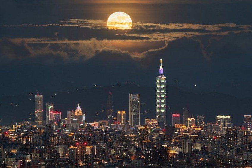 A city skyline at night with a prominent tower illuminated, a full moon in the sky, and clouds. 2