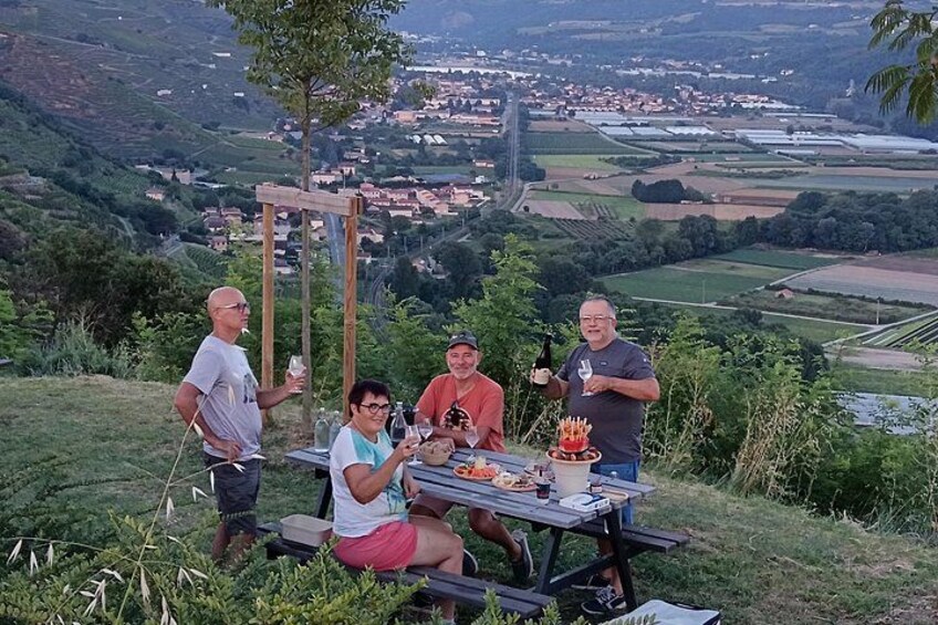 A group of people at a picnic table with a scenic view of a valley and houses in the background. 3