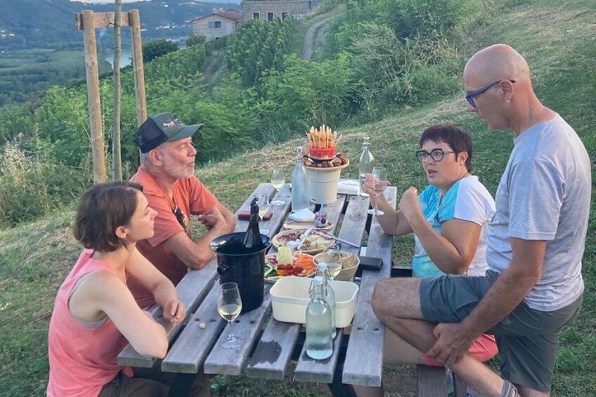 A group of people sitting at a picnic table outdoors with food and drinks. 2