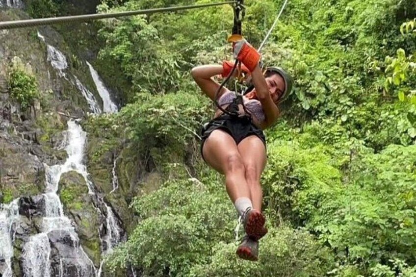 A person zip-lining through a forest with a waterfall in the background. 4