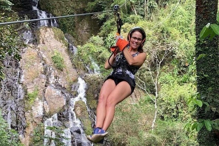 A person zip-lining over a waterfall in a forested area. 5