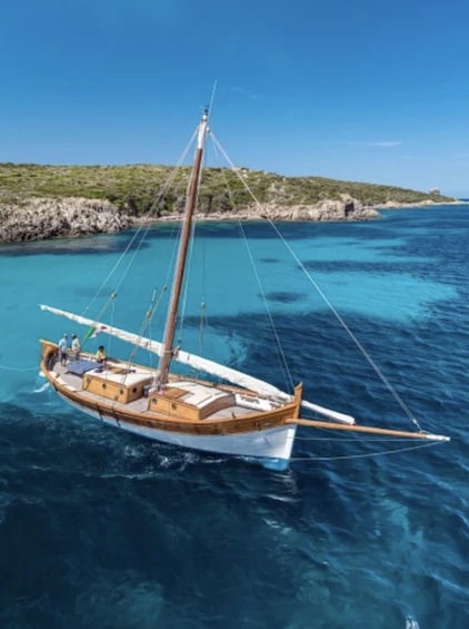 A sailboat on clear turquoise waters with rocky coastline and greenery in the background. 2