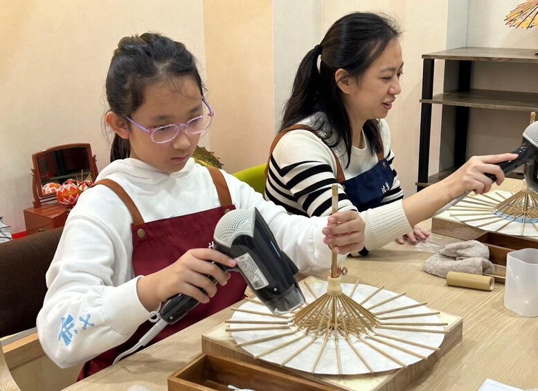 Two people working with a hairdryer and wooden sticks on a table. 3