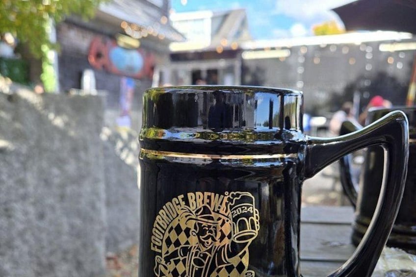 Eine schwarze Tasse mit goldener Schrift und Henkel, draußen auf einer Oberfläche platziert. 3