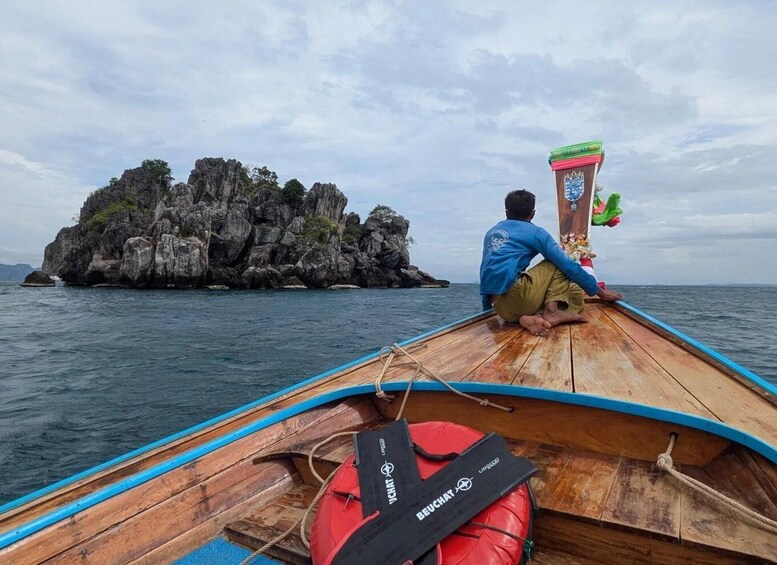 A person sitting on a wooden boat with a rocky island in the background. 5