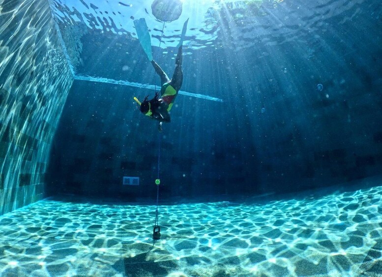 A diver underwater in a clear pool with a sandy bottom and a rope descending. 2