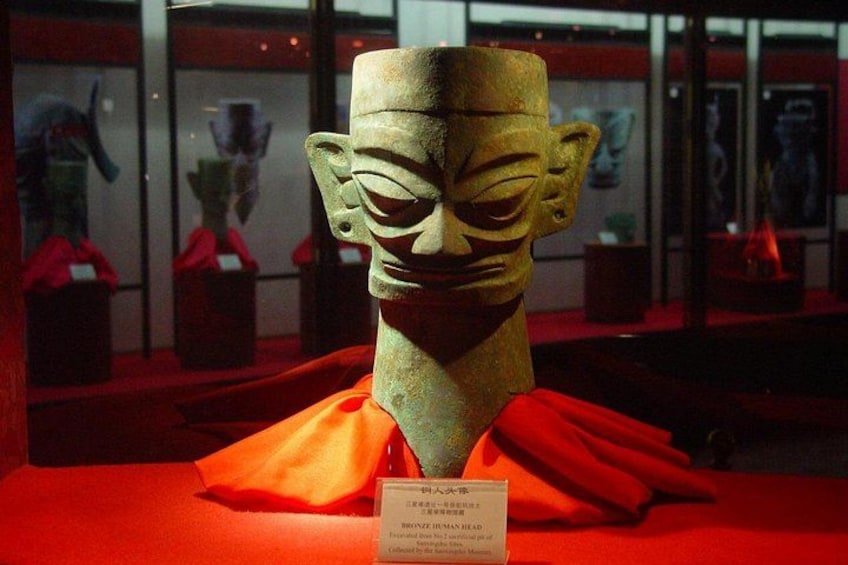 A museum display with a bronze head sculpture on a red cloth. 1