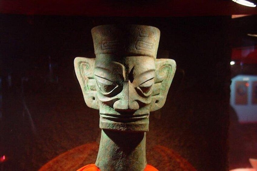 A bronze statue with a detailed face and headdress, displayed in a museum setting. 2
