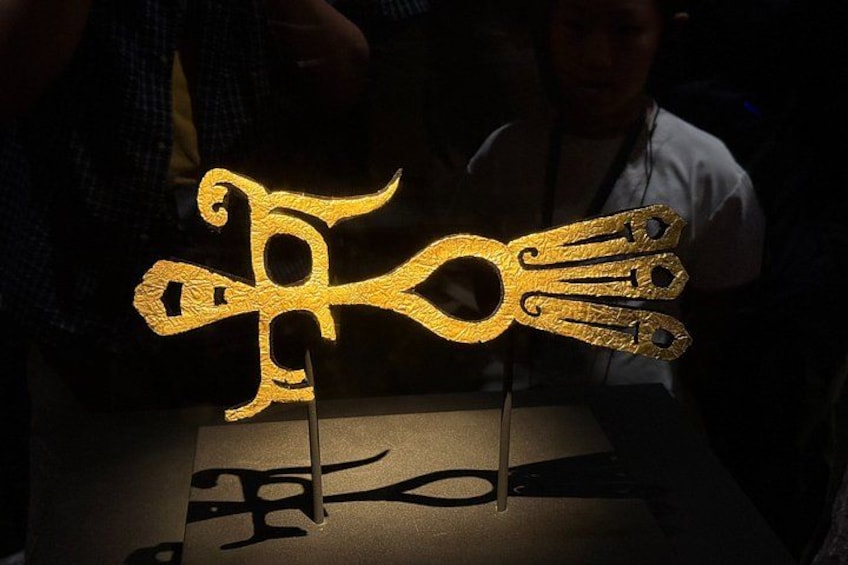A golden decorative object with a unique design, possibly a piece of jewelry or an ornament, displayed on a stand. 4