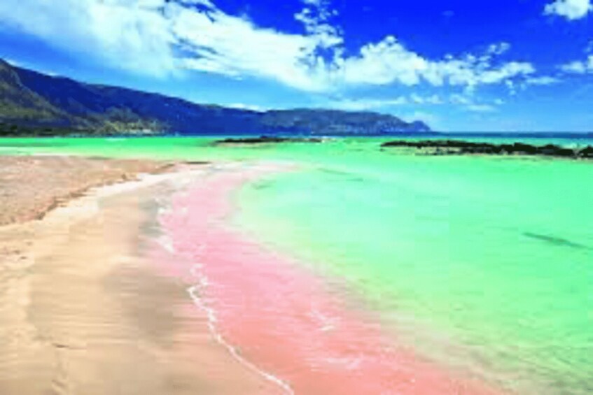 A beach with clear turquoise water, a pink sand area, and mountains in the background. 2