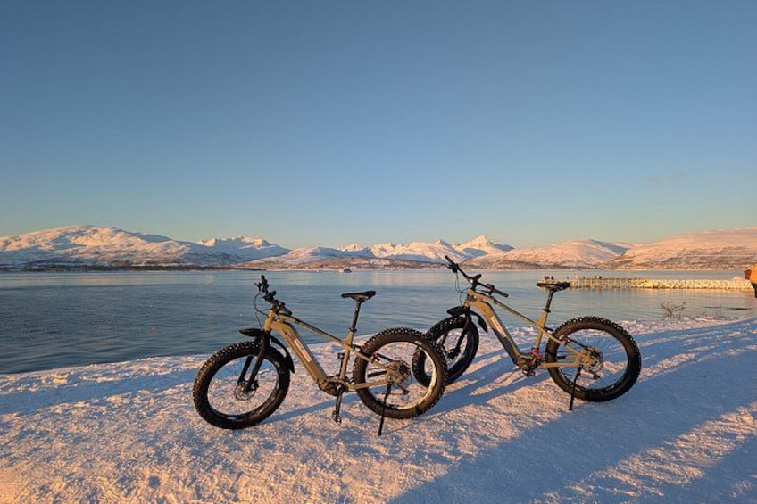 En mountainbike parkeret på en sneklædt strand med en sø og bjerge i baggrunden. 1