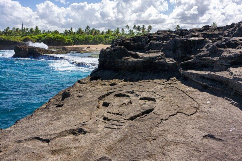 A rock formation with a carved face and footprints near a coastal area with waves and palm trees. 2